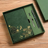A dark green box containing a luxury notebook set with gold accents and a black pen on a wooden surface.