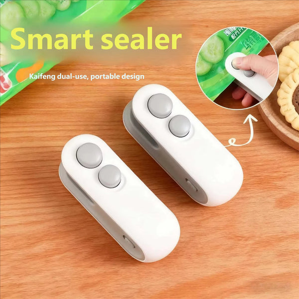 Selladora de calor USB recargable blanca y portátil con dos botones sobre una superficie de madera junto a pepinos rebanados.