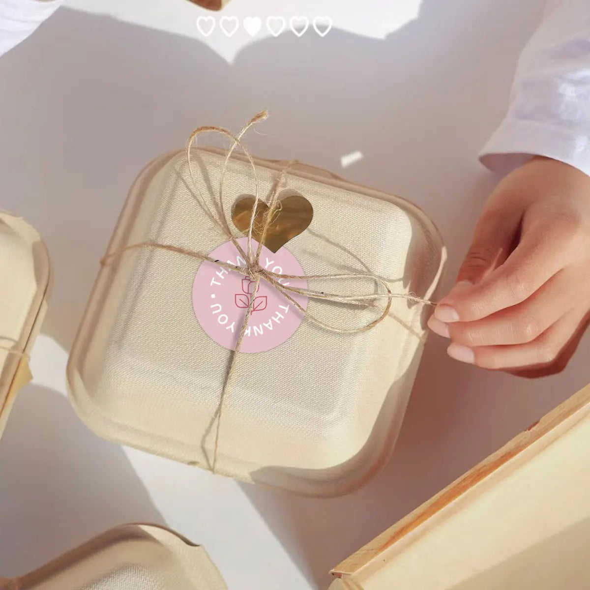 A light beige thank you sticker roll tied with twine and a gold heart on a white background.
