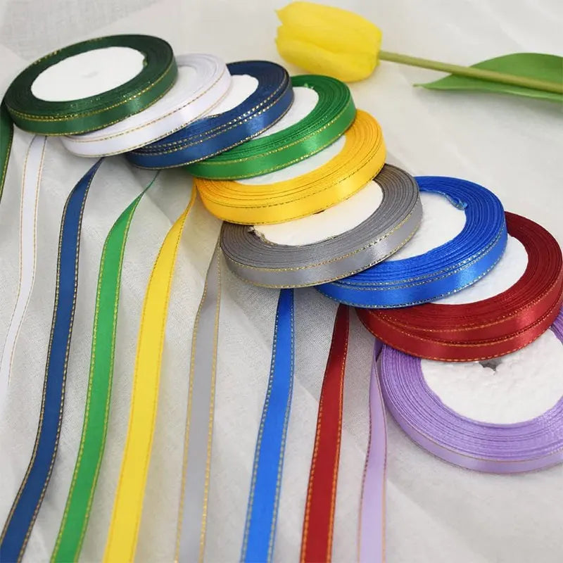 A collection of gold edge satin ribbons in various colors including green, white, blue, yellow, and red, laid out on a white 