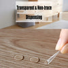 Une main applique un point de décoration adhésif double face transparent sur une surface en bois.