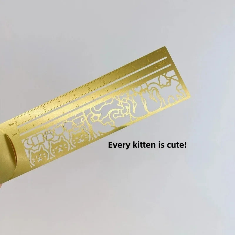 Marcador de metal dorado con diseños intrincados de gatos y marcas de medición.