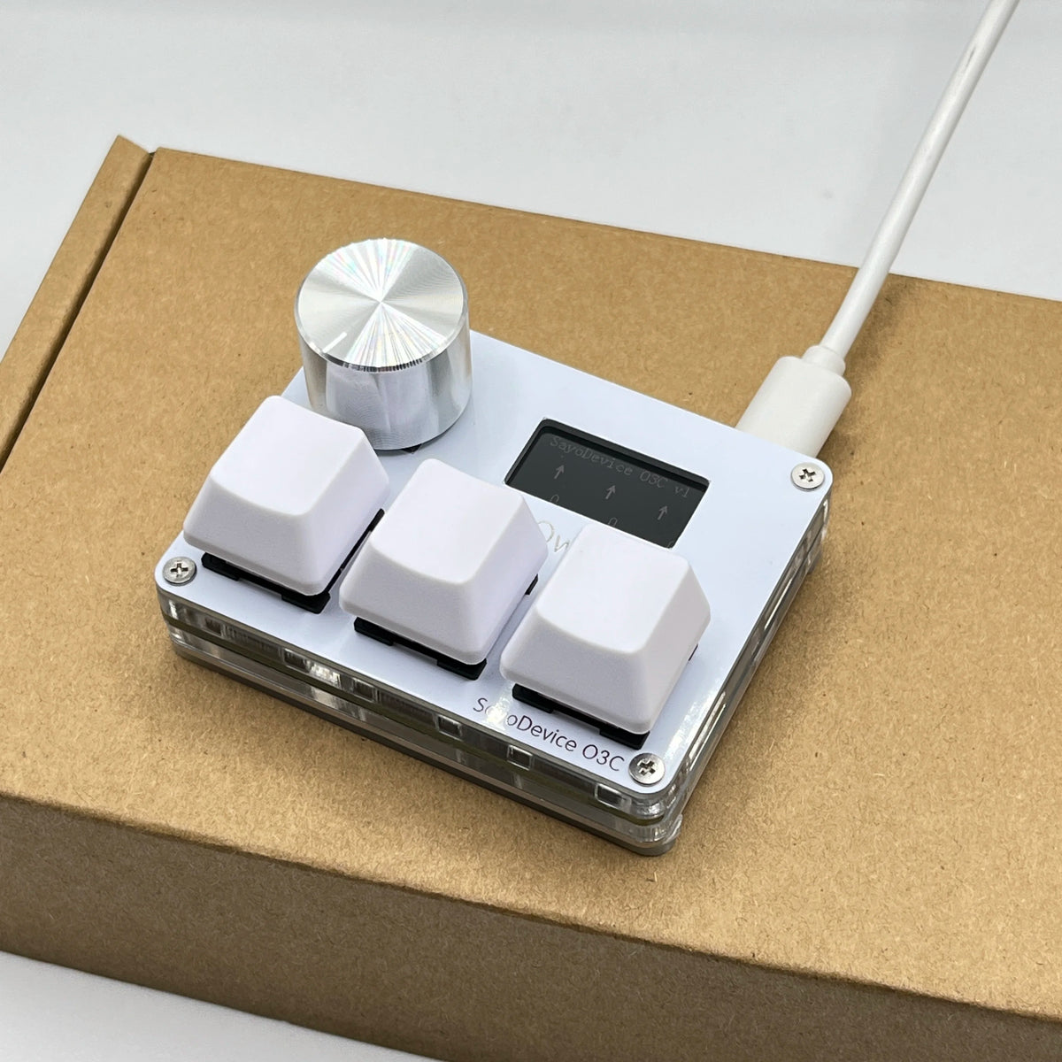 A white electronic device with a silver magnetic top and a white cable is placed on a brown cardboard box.
