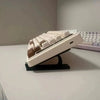 A white ergonomic keyboard height adjuster stand holding a row of white keyboard keys.