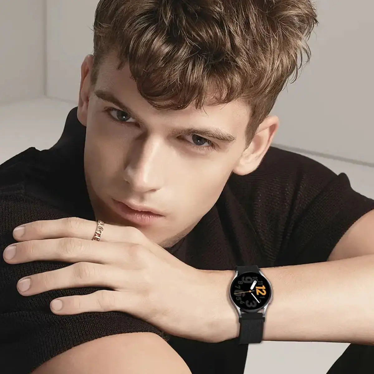 A young man wearing a black shirt holds a black smartwatch on his wrist.