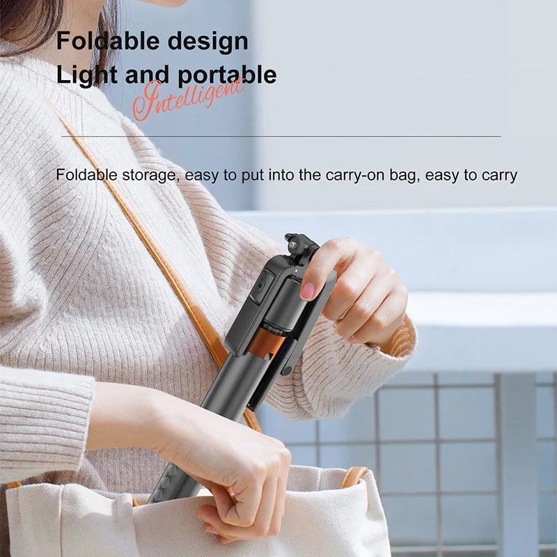 A person is holding a foldable design AI face tracking smartphone tripod with Bluetooth remote in a light beige sweater.