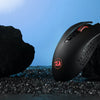 A black Redragon wireless gaming mouse is placed on dark gravel next to large rocks under a blue sky.