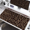 A large leopard print desk pad is displayed on a white desk next to a computer monitor and a mug.