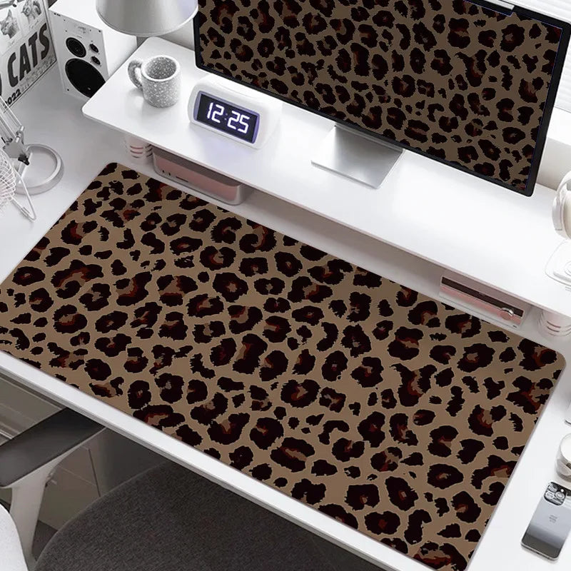 A large leopard print desk pad is displayed on a white desk next to a computer monitor and a mug.