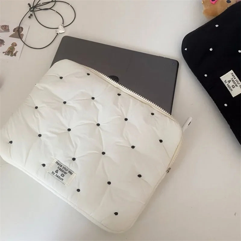 A white quilted padded laptop sleeve case is shown next to a dark laptop and a black fabric item.