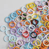 A collection of colorful spring clasps in various colors like yellow, orange, pink, and blue arranged on a light gray surface