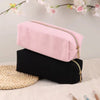 A pink ribbed pencil case resting on a black one next to a woven mat with floral branches in the background.