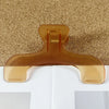 A clear, translucent book page clip in a warm amber color resting on a textured brown surface.