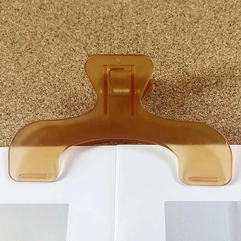 A clear, translucent book page clip in a warm amber color resting on a textured brown surface.