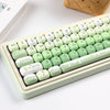 A close-up of a light green PBT keycap set featuring various characters and modifiers, displayed on a white surface.