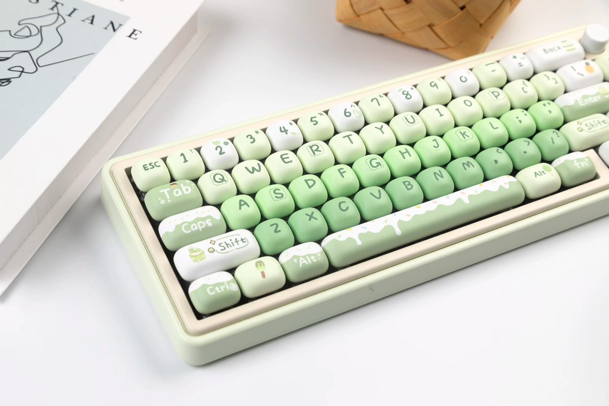 A close-up of a light green PBT keycap set featuring various characters and modifiers, displayed on a white surface.