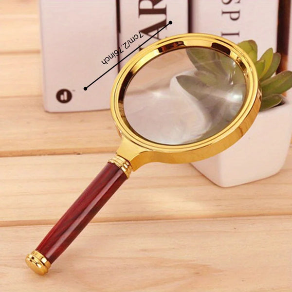 A gold-rimmed magnifying glass with a reddish wooden handle is shown next to a white box.