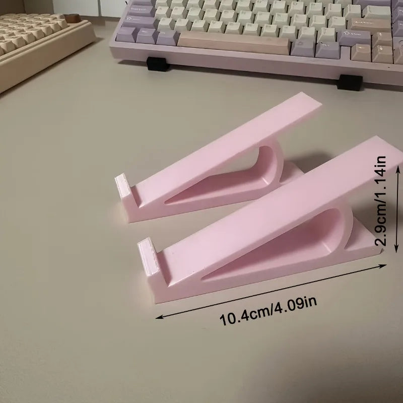 Two pink ergonomic keyboard riser stands with anti-slip bases shown on a light floor.