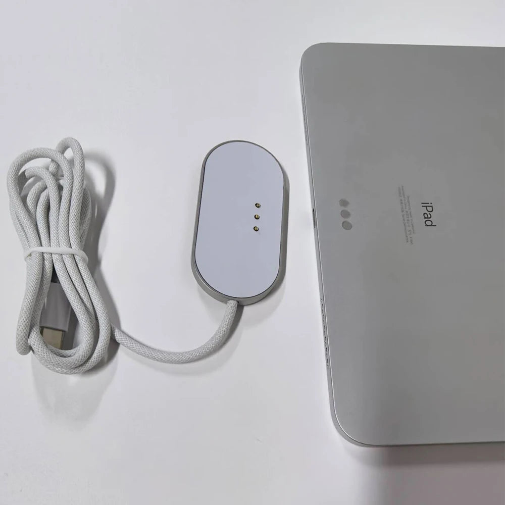 A silver magnetic wireless charging adapter and cable next to a white iPad.