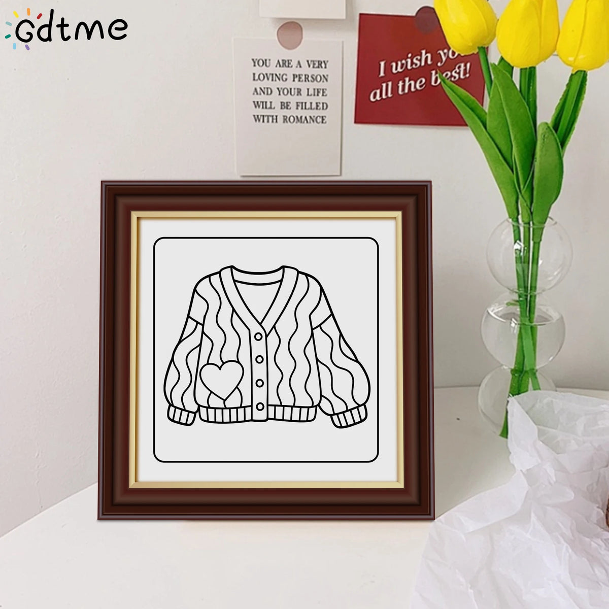 A framed black and white line art drawing of a sweater with a heart pattern on a white background
