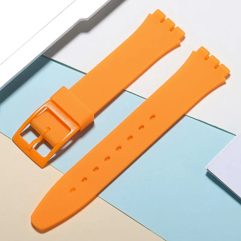 An orange soft silicone watch strap is shown next to its replacement tools on a light background.