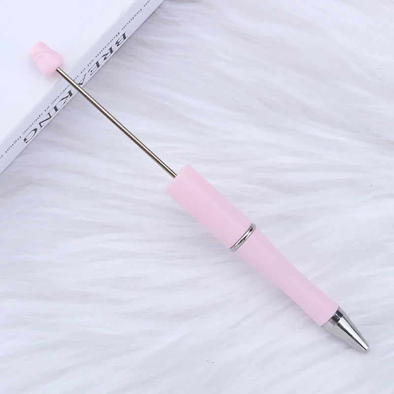 A pink DIY beadable pen with a silver tip is shown resting on a white, fluffy surface.