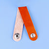 A single piece of orange faux leather material is shown next to a light wood-toned piece on a blue background.