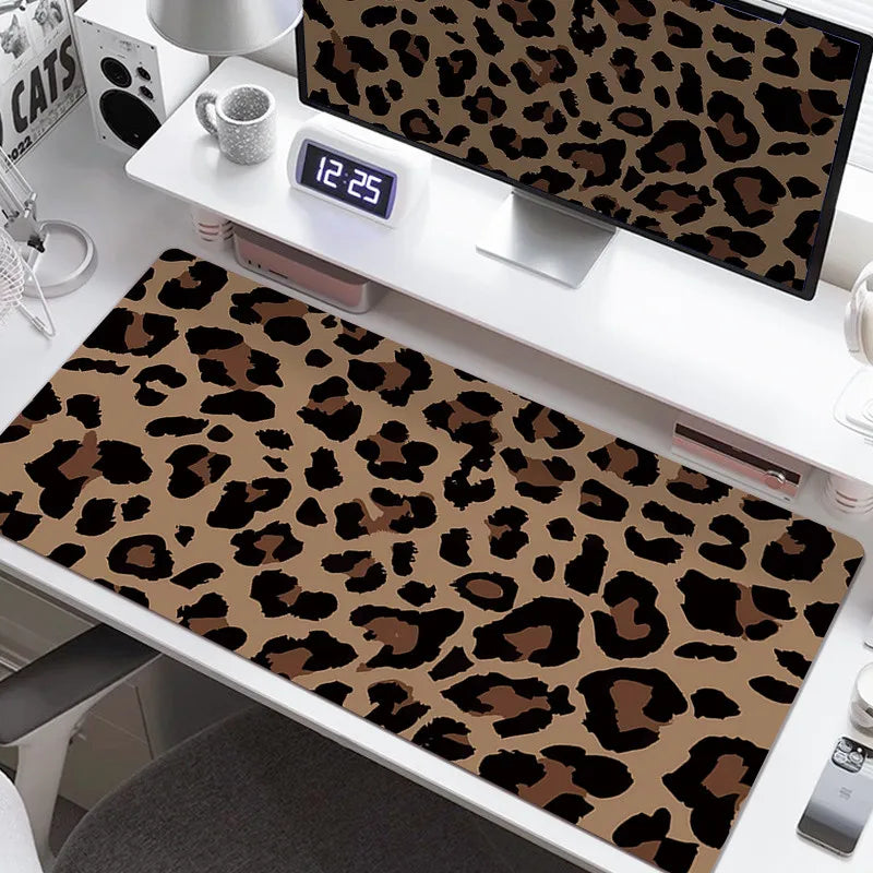 A large leopard print desk pad is displayed on a white desk next to a monitor and a clock.