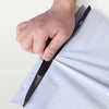 A hand is sealing a white dustproof mailing bag with a black sealing strip.