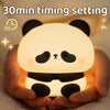 A hand is holding a cute panda silicone night light with a warm glow.