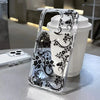 A clear phone case with a black floral pattern is placed next to a white cup.