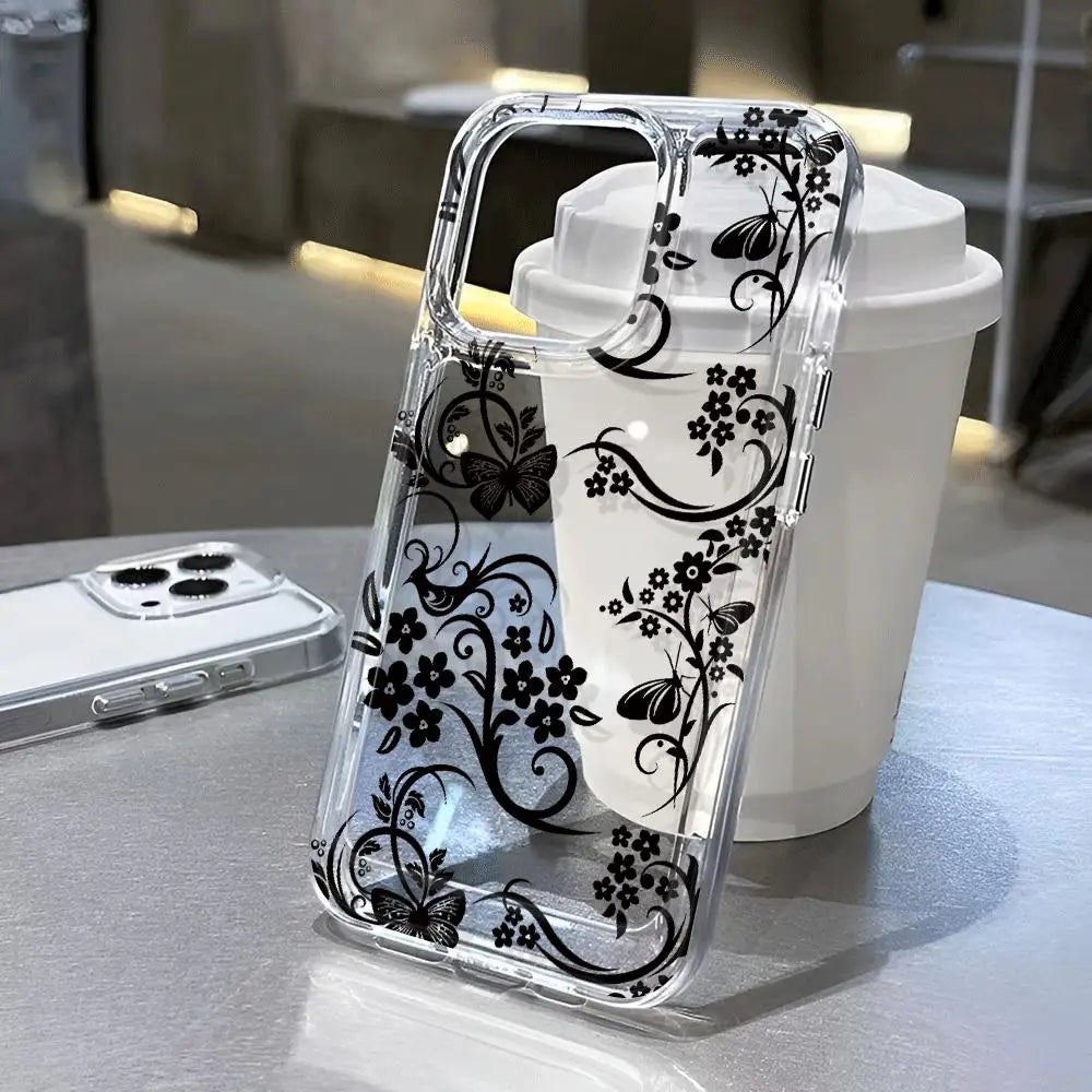 A clear phone case with a black floral pattern is placed next to a white cup.