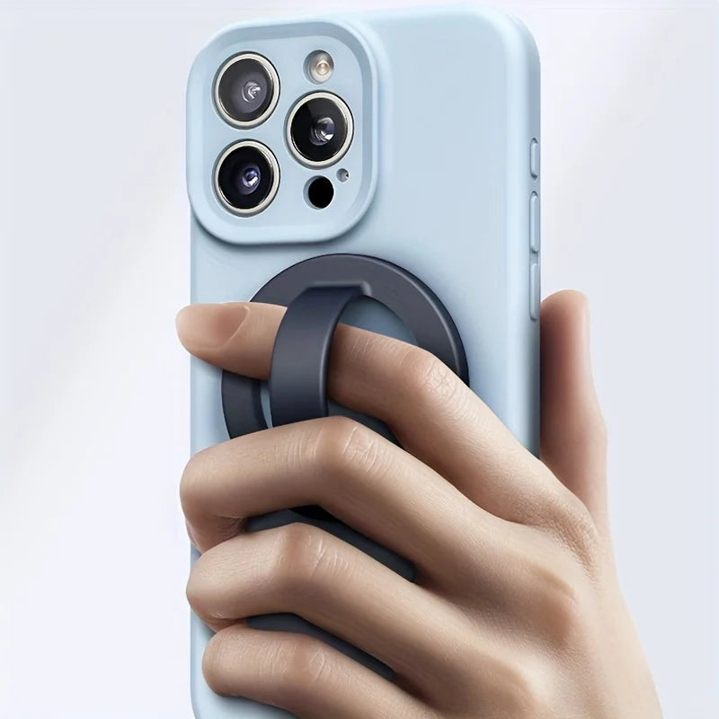 A hand holds a light blue magnetic silicone phone grip with a foldable stand.