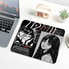 A black mouse pad featuring a Junji Ito Tomie design with stitched edges, placed next to a laptop and a small tin.