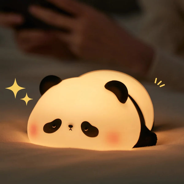 A glowing white silicone panda night light rests on a surface, with a hand visible in the background.