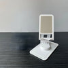 A white desktop stand for a phone or tablet with a mesh grille, resting on a dark surface.