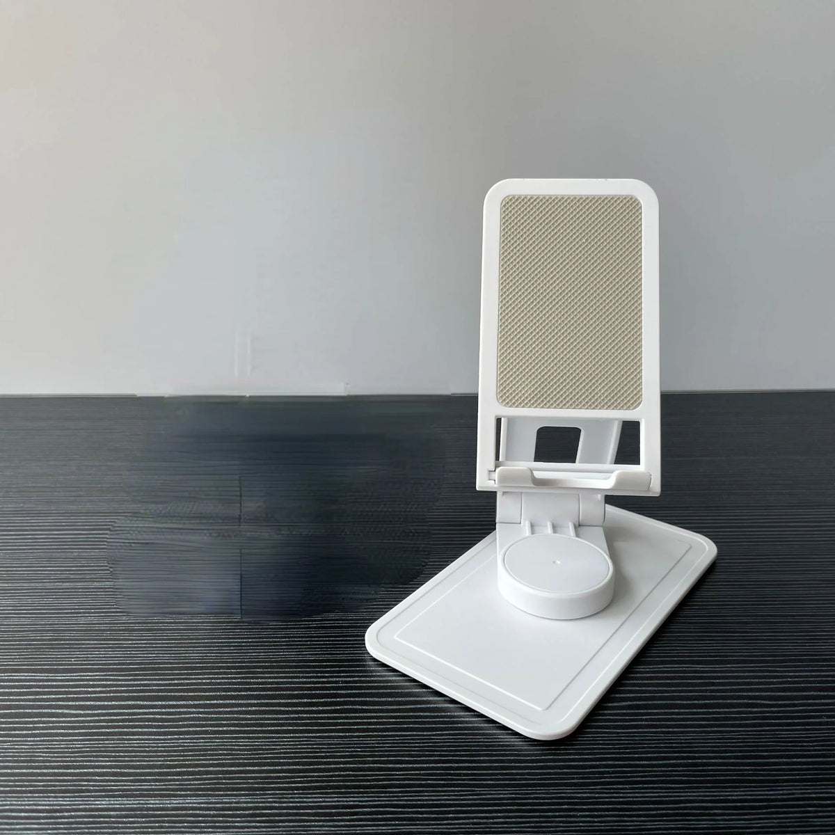 A white desktop stand for a phone or tablet with a mesh grille, resting on a dark surface.