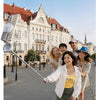 A woman holds a selfie stick extending to 1.46m for group selfies in front of historic European architecture.