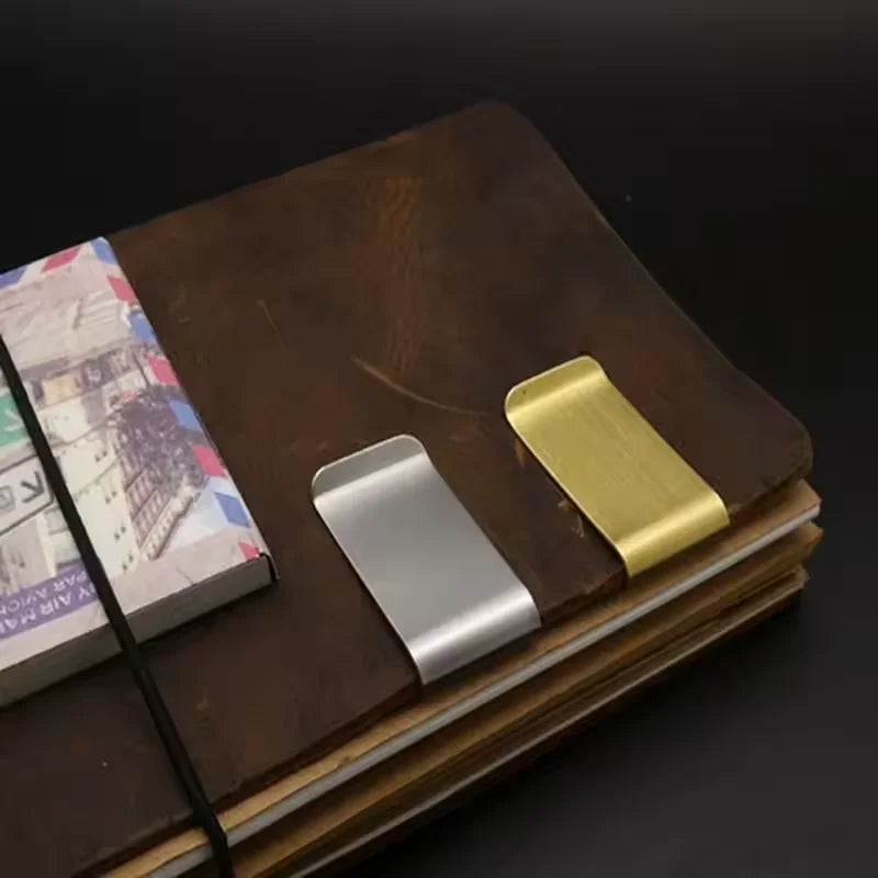 A vintage solid brass money clip with a card holder resting on a dark brown leather-bound book.