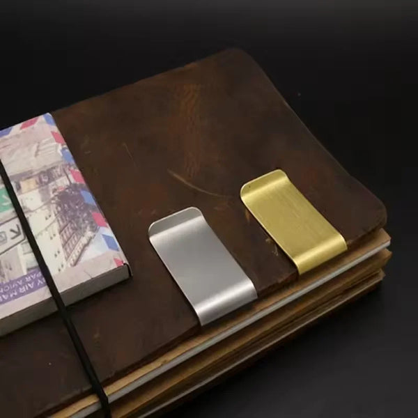A vintage solid brass money clip with a card holder resting on a dark brown leather-bound book.