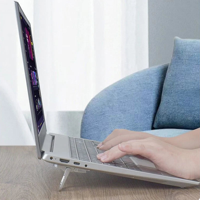 A silver laptop is resting on a wooden table with a person's hand near the keyboard, set against a bright background.