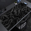 Extra large abstract desk mat with black and white topographic lines on a dark surface.