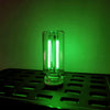 A glass bulb with a bright white LED filament is illuminated against a green background on a metal grid.
