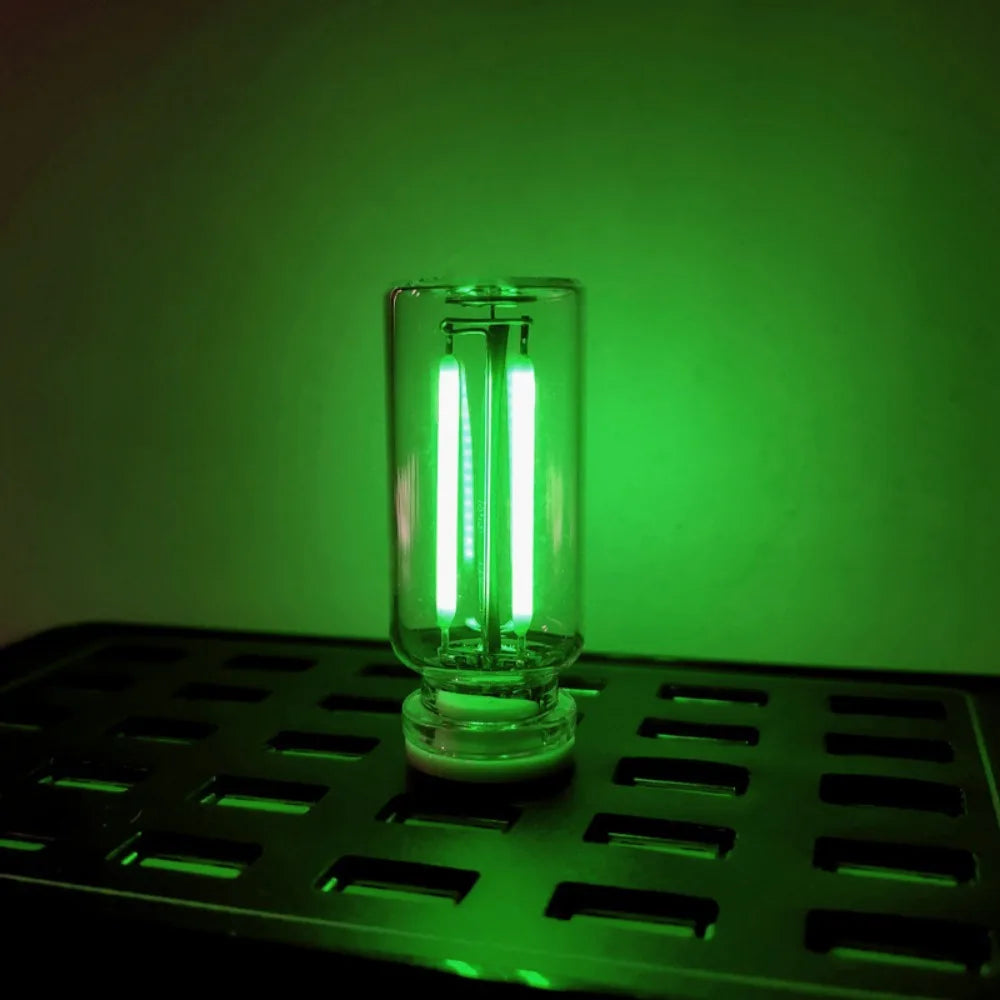 A glass bulb with a bright white LED filament is illuminated against a green background on a metal grid.