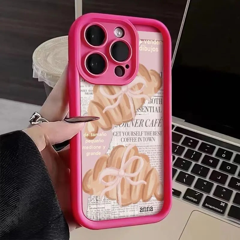 A pink phone case with a croissant newspaper pattern is shown next to a hand and a laptop.