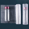A clear glass bottle with a pink cap is shown next to two rolls of thick bubble wrap packaging.
