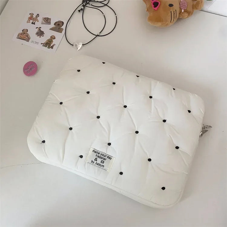 A white quilted padded laptop sleeve case with black studs is shown on a white surface.