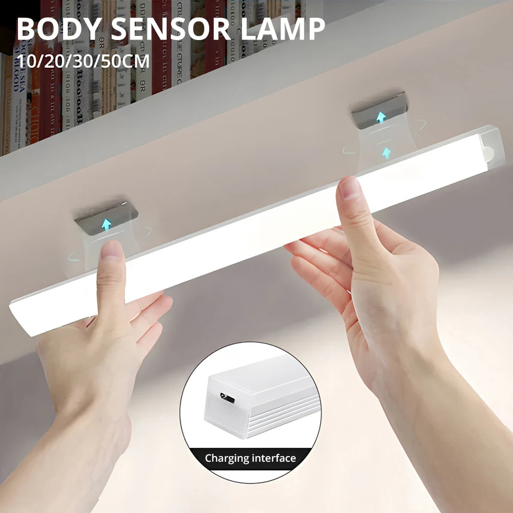 Hands hold a white body sensor lamp light strip illuminating a surface, showing the charging interface.