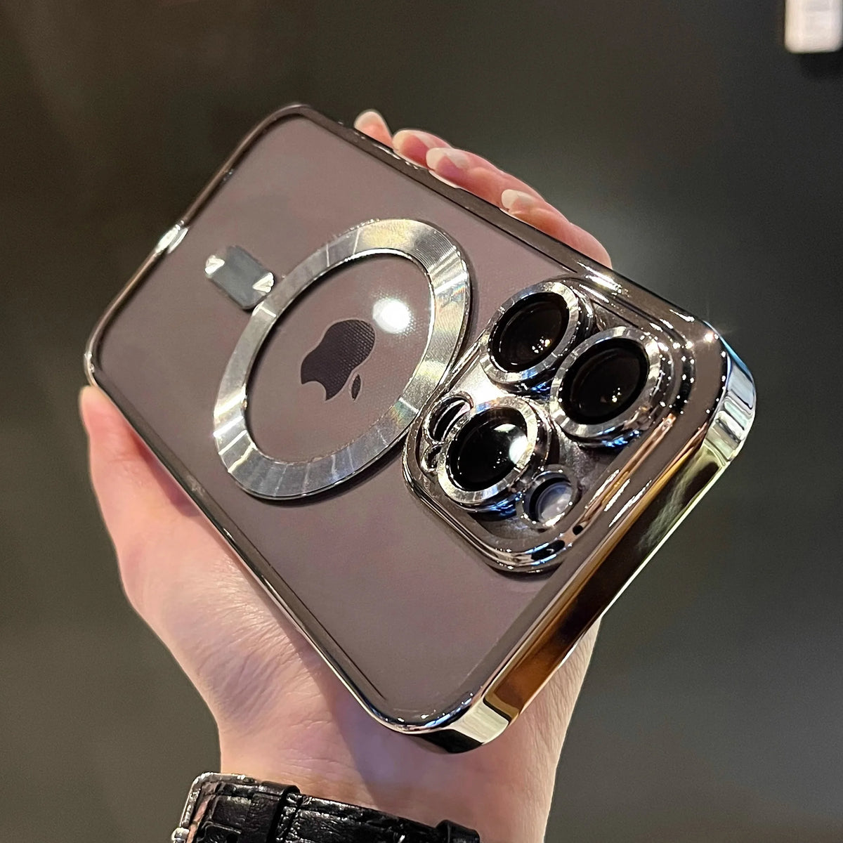 A hand holds a clear magnetic case with a plated finish for a MagSafe iPhone.