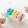 Una mano sostiene una cortadora y dispensador de cinta washi de varios estilos y colores dentro.